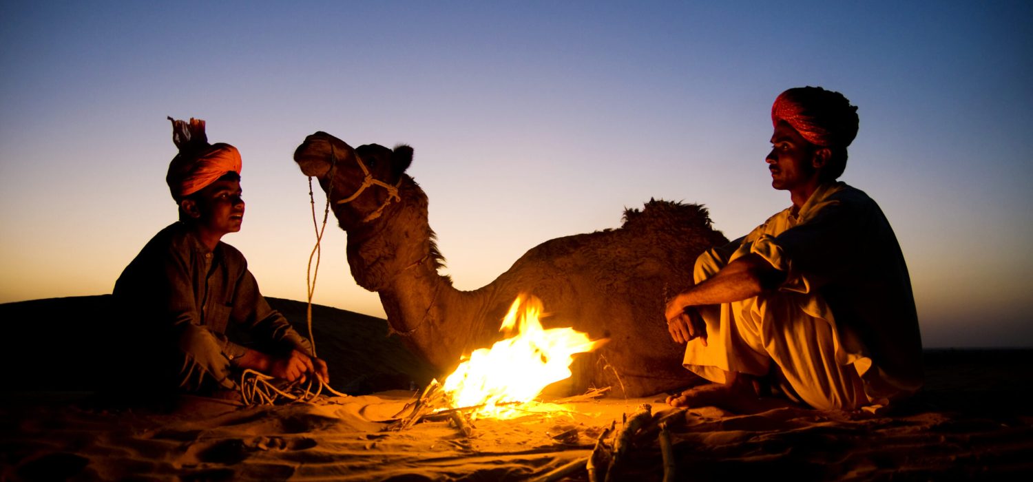 Indian men resting by the bonfire with their camel